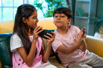 Indian Asian siblings kids using smartphones for mobile games while enjoying fun at home together