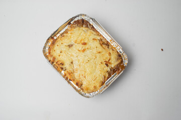 Homemade lasagna in aluminum container top view on white background