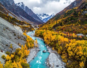 Turquoise river winds through a valley of autumnal trees nestled between snow-capped mountains under a cloudy sky