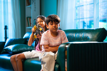 Indian sibling kids fight over toy bike on sofa, one upset in modern home atmosphere