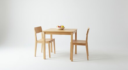 A lightwood table set with two chairs featuring a bowl of fruit atop the table against a plain white background