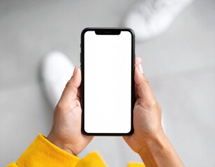 Overhead view of hands holding a blank white smartphone screen, with white sneakers blurred in the background, focusing on the display