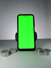 Picture of a phone showing green screen and stack of coins in sides. This photo can be used for Economy or money related advertisement