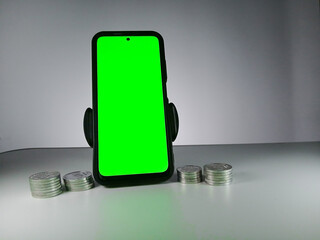 Picture of a phone showing green screen and stack of coins in sides. This photo can be used for Economy or money related advertisement