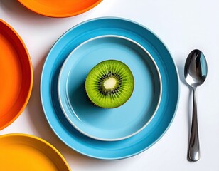 Vivid, minimalist flat lay Half kiwi on blue plate beside a spoon, amid orange and yellow plates, on a bright, clean white background