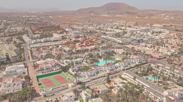 Aerial panorama revealing white architecture, tennis court, swimming pools, palm trees against volcanic terrain in Costa Calma, Fuerteventura, Canary Islands, Spain