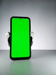 Picture of a smartphone showing green screen with earphones attached. This photo is taken with white background. This photo can be used for musical theme advertisement or music related promotion
