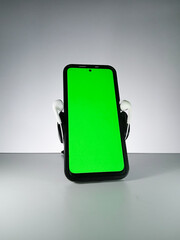 Picture of a smartphone showing green screen with earphones attached. This photo is taken with white background. This photo can be used for musical theme advertisement or music related promotion
