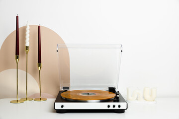 A vinyl record player with a transparent dust cover and a marbled orange record is the main focus of this minimalist setup. Surrounded by decorative candles and wooden accents, it creates a stylish an © romanovad
