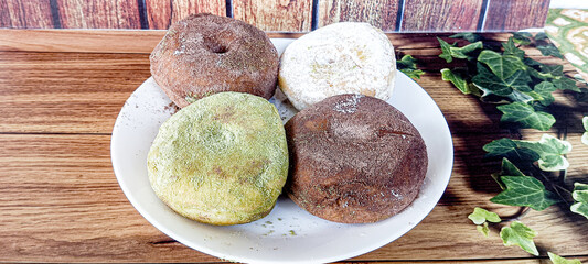 Two milk chocolate donuts, one matcha donut, and one sprinkled sugar donut are served on a white...