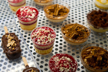 Assorted desserts in cups with layers of cream, fruit, and biscuits, alongside chocolate-covered ice cream bars, beautifully displayed on a metal tray.             