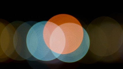 Abstract bokeh with overlapping orange and blue circles of light on a dark background, creating a dreamy artistic night effect.