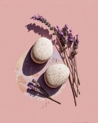 Two light beige stones, surrounded by lavender sprigs on a pale pink surface