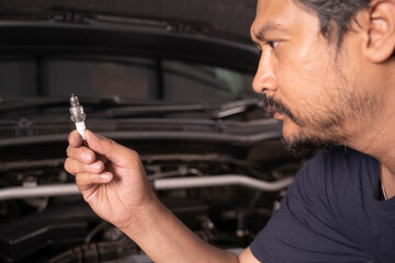 A middle-aged Asian mechanic works under the hood of a car.