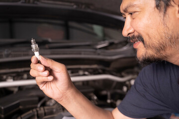 A middle-aged Asian mechanic works under the hood of a car.
