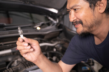 A middle-aged Asian mechanic works under the hood of a car.