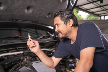 A middle-aged Asian mechanic works under the hood of a car.