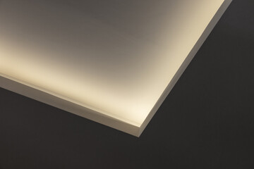 A minimalist interior close-up shows warm indirect lighting along an angled ceiling