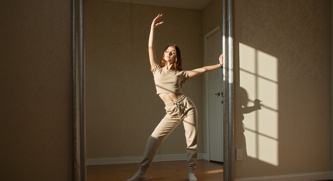 Young woman dancing gracefully in a sunlit room by a mirror