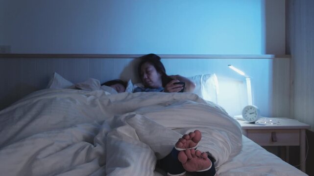 Asian single mum is sleepless, restless leg syndrome, is stressed, worried, awake at night near her child, with insomnia illness, mature and menopausal woman, family healthcare lifestyle problem.