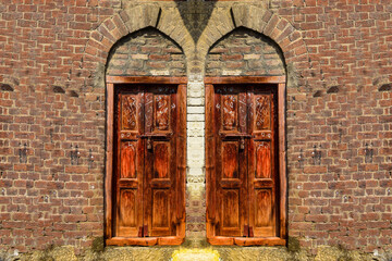 A beautiful old wooden door on stone wall background, old entrance wooden double-leaf brown door with wrought iron decor, old door building exterior detail