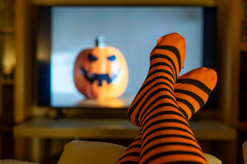 Cozy home lifestyle with striped socks, blurred pumpkin decoration and Halloween streaming...