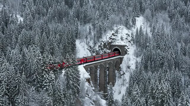 Red train crossing a snowy viaduct and entering a tunnel