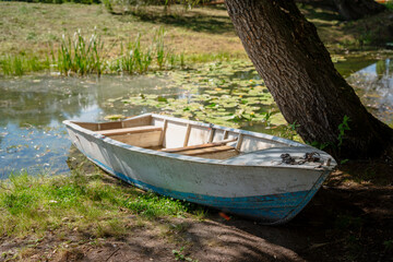 Obraz premium A lonely boat on the bank of a river or pond in summer