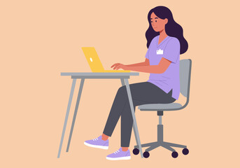 Woman working on laptop at desk wearing scrubs sitting on chair.
