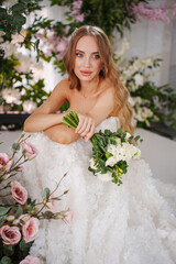 Beautiful bride with long blonde hair sitting surrounded by flowers. 