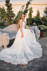 Beautiful bride with long blonde hair on a stone bench in an evening park. 