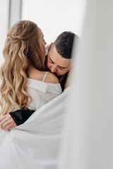 A gentle and romantic man and woman wrapped in a blanket on the windowsill