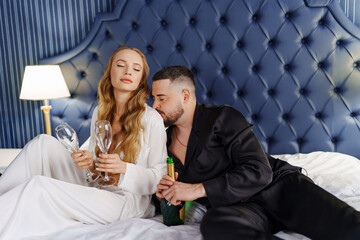 A man and a woman in silk pajamas with champagne are lying on a bed.