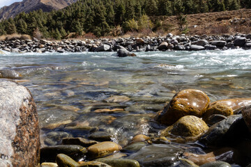 Close up view of clear river with sunlight reflecting on colorful stones and pebbles under the water. The natural ripples and shimmering light patterns create a peaceful and refreshing atmosphere.