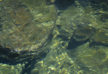 Fototapeta premium Sun-Dappled Riverbed: Reflections and Submerged Stone Textures