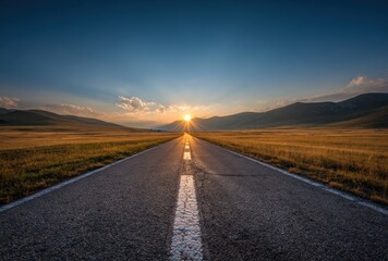 Fototapeta premium Straight asphalt road leads to horizon at golden sunset in a grassland valley. Blue sky above