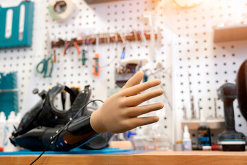 A realistic robotic arm rests on a workbench. Tools hang on the wall. This shows technology being used to improve the lives of disabled people
