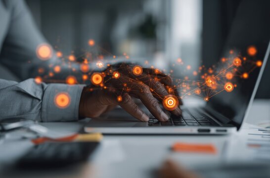 Man typing on a laptop with glowing orange digital network overlay, set on a clean white desk in a blurred office environment - Powered by Adobe
