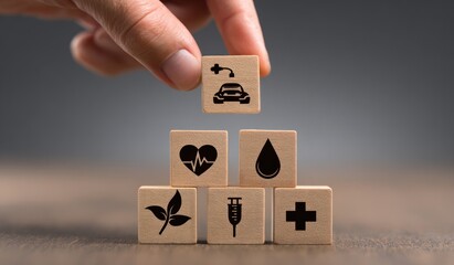 Hand places a block with an electric car symbol atop a stack of health-related blocks on a wooden surface against a blurred grey backdrop
