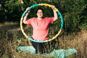 A plus-size woman is doing gymnastics in nature. A woman with a hoop in her hands. Outdoor sports. 