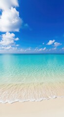 Obraz premium Serene view of a tropical beach with clear turquoise water meeting the white sandy shore under a bright blue sky with fluffy clouds.