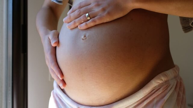 Self-massage for pregnant women. Pregnant woman apply cream or oil to their belly to help prevent or reduce stretch marks and to soothe dry, itchy skin. Eight months pregnant.