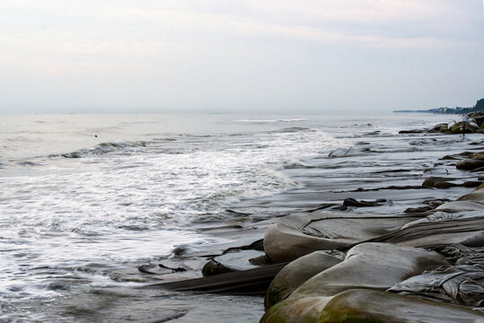 Coastal Shoreline With Weathered Tarps and Rocky Beach Under Quiet Gray Sky - Powered by Adobe