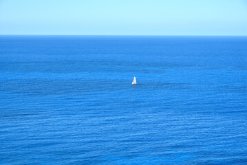 View of the open sea with blue sky and sailing boat in the distance