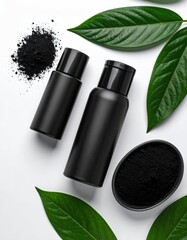 Two black cosmetic bottles, charcoal powder, and vibrant green leaves arranged on a white background; minimalist aesthetic