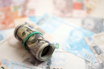 Roll of US dollar bills lies on big amount of Brazilian reais banknotes close up