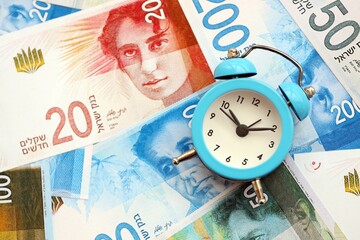 Israel New Shekels banknotes and alarm clock. The current Israel money bills and clock lies on table