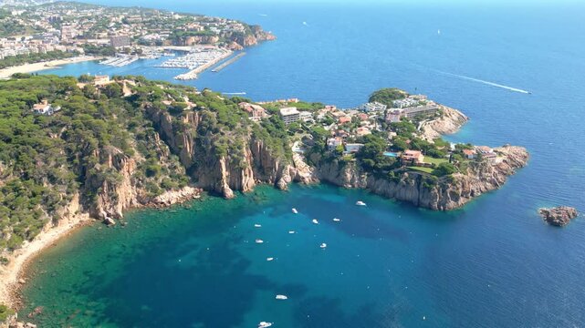 Amazing aerial perspective of the rugged coastline and clear turquoise water of sant feliu de guixols on the costa brava, showing luxury villas, boats, and the distant city marina