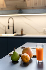 Carrot juice glass with citrus by cutting board in stylish kitchen. Vitamin mood.