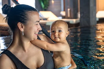 Mom and baby in spa pool, gentle cuddle and droplets. Closeup of care.